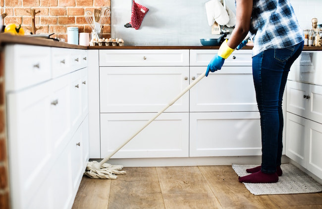 An image of person cleaning with a broom in the kitchen